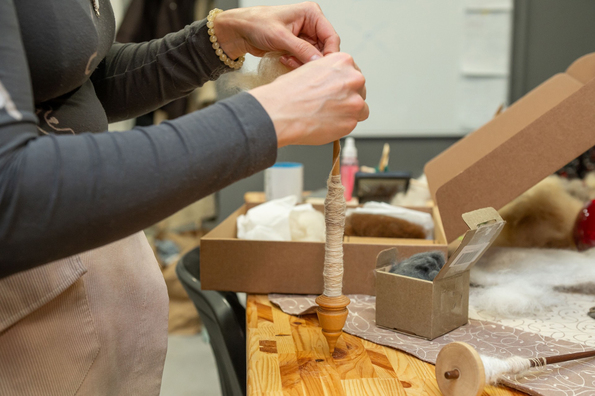Female adult hand crafting yarn with spindle in workshop